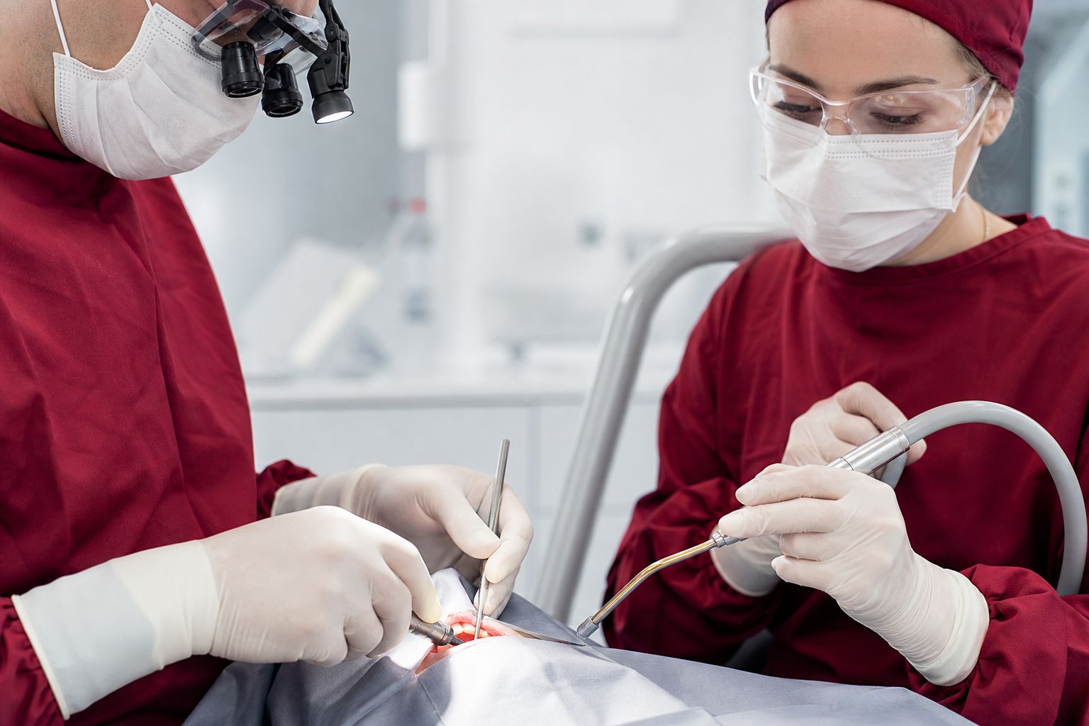 Ein Oralchirurg führt eine Zahnfreilegung durch, während eine Assistenz den Eingriff professionell begleitet.